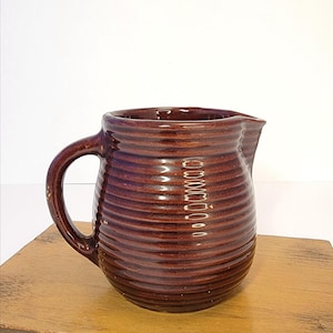 May include: A white ceramic mug with a black handle and the text "But First, Coffee" in a bold, black font. The mug is set against a blurred background, suggesting a cozy setting.