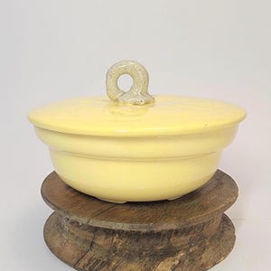 May include: A white ceramic mug with a black handle and the text "But First, Coffee" in a bold, black font. The mug is set against a blurred background, suggesting a cozy setting. The mug appears to be approximately 4 inches tall.