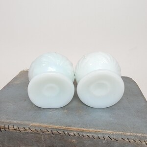 May include: Two white, vintage, swirl-patterned glass dessert dishes. Each dish has a round base and a bowl-shaped top. The dishes are displayed on a gray surface.