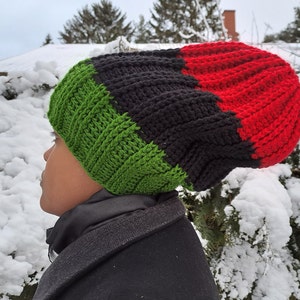 May include: A green, black, and red knitted beanie hat. The hat is slouchy and has a thick knit.