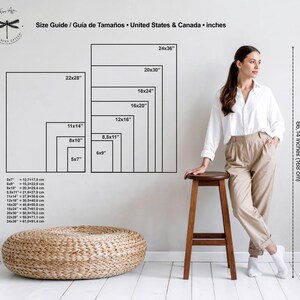May include: A size guide graphic displays various rectangular art print sizes in inches, with corresponding metric measurements. A woman stands near a wooden stool, and a woven ottoman sits on the floor. The text reads "Size Guide / Gu&iacute;a de Tama&ntilde;os &bull; United States & Canada &bull; inches."