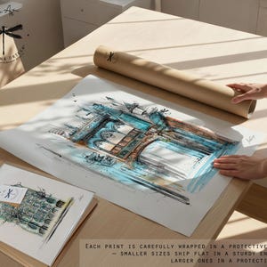 May include: An architectural watercolor print with blue and brown tones, alongside a smaller print and a rolled tube. The larger print is being handled on a light wood surface. The text on the image says "Each print is carefully wrapped in a protective sleeve - smaller sizes ship flat in a sturdy envelope, larger ones in a protective tube."