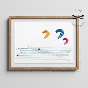 May include: Watercolor painting of kitesurfing. The artwork features three colorful kites in the sky: yellow, blue with stripes, and pink. The ocean is depicted with blue brushstrokes, and there are small figures of people kitesurfing. The artwork is framed in a wooden frame.