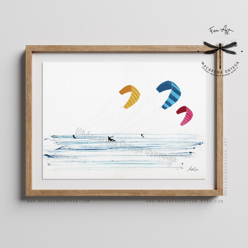 May include: Watercolor painting of kitesurfing. The artwork features three colorful kites in the sky: yellow, blue with stripes, and pink. The ocean is depicted with blue brushstrokes, and there are small figures of people kitesurfing. The artwork is framed in a wooden frame.