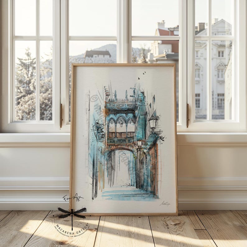 May include: Watercolor painting of a European street scene in a wooden frame. The artwork features a blue arched bridge and buildings with architectural details. The painting has a light color palette with blue and brown tones. The artist's signature is visible.