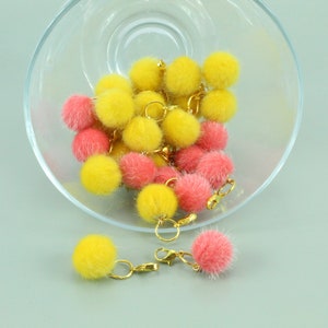 Pode incluir: Uma tigela cheia de pompons fofinhos rosa e amarelos com fechos de metal dourado.
