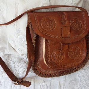 May include: A brown leather shoulder bag with intricate embossed floral designs. The bag has a flap closure and a long adjustable strap.