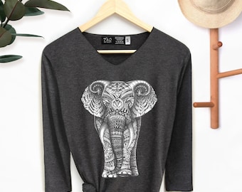 Puede incluir: Una camiseta gris oscuro de manga larga y cuello en V con un gráfico blanco de un elefante con intrincados patrones de mandala. La camiseta tiene un dobladillo anudado y la etiqueta de talla dice "S".