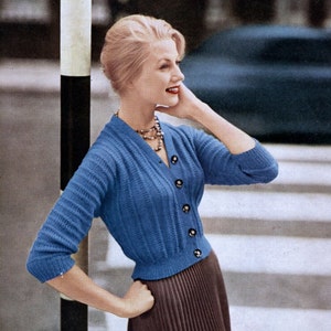 May include: A blue knitted cardigan with a V-neck and button closure. The cardigan has a ribbed texture and is fitted at the waist.