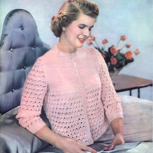 Könnte beinhalten: Ein rosa gestrickter Cardigan mit Knopfleiste und zartem Spitzenmuster. Der Cardigan wird von einer Frau mit einer Frisur im Stil der 1950er Jahre getragen.