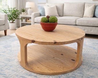 May include: A round, light-toned wooden coffee table featuring a smooth circular top and a matching circular lower shelf supported by four curved, integrated legs. The natural wood grain and visible knots are present throughout the structure.