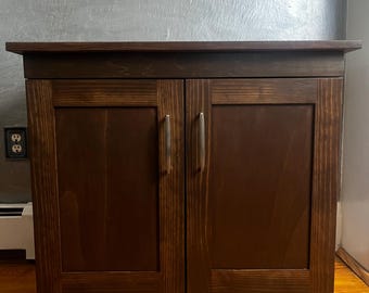 May include: A dark brown wooden cabinet with two doors and silver handles. The cabinet has a simple design and is made of solid wood.