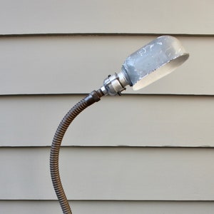May include: A vintage industrial style desk lamp with a flexible metal arm and a gray metal shade. The lamp has a black cord and a round base.