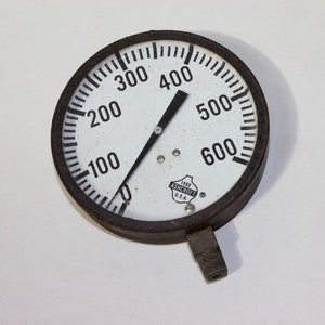 Pu&ograve; includere: Un manometro rotondo bianco con un ago nero che punta a 400. Il manometro ha un quadrante nero con numeri e segni bianchi. Il manometro &egrave; etichettato "1000 ASHCROFT U.S.A."