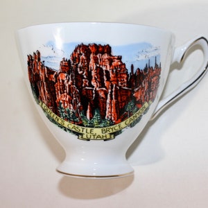 May include: White porcelain teacup with a colorful image of Queen's Castle in Bryce Canyon, Utah.