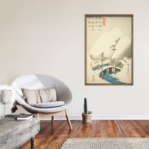 Op de afbeelding: Een ingelijste Japanse houtsnede die een besneeuwd berglandschap met een brug over een rivier afbeeldt. De print is in tinten blauw, wit en grijs, met een paar accenten in bruin en zwart. De print is getiteld "雪景" in Japanse karakters, wat zich vertaalt naar "Sneeuwlandschap".