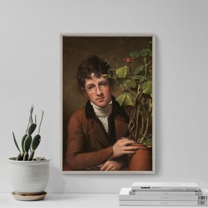 May include: Framed portrait of a man in a brown coat and glasses, holding a potted plant with green leaves and red flowers. The artwork has a vintage aesthetic, with a neutral background and a white border.