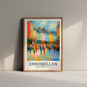 May include: A framed art print featuring an impressionistic painting of a vibrant street scene in Enniskillen, County Fermanagh. The artwork displays colorful buildings and a crowd of people in a painterly style, with the text ENNISKILLEN COUNTY FERMANAGH.