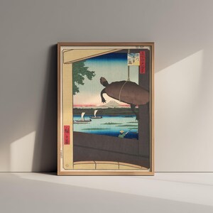 Op de afbeelding: Een ingelijste ukiyo-e houtsnede met een grote donkere schildpad die aan een touw op de voorgrond hangt. De scène toont een rivier met zeilboten, een verre berg en een persoon in een boot. Japanse tekst is zichtbaar op de rode randen.