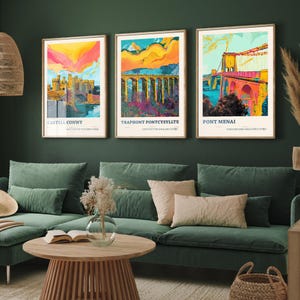 May include: Three framed wall art prints featuring vibrant, stylized illustrations of Welsh landmarks. The left print shows Castell Conwy, the center print depicts Traphont Pontcysyllte, and the right print displays Pont Menai, all with bold, colorful skies.