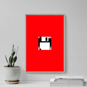 Könnte beinhalten: Ein gerahmter Kunstdruck mit einem kräftigen roten Hintergrund und einer schwarz-weißen Grafik einer Diskette. Das Kunstwerk ist minimalistisch und modern, mit einem Retro-Tech-Thema. Der Druck ist in einem hellen Rahmen eingefasst.