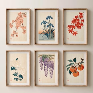 May include: A set of six framed vertical wall art prints featuring botanical illustrations on a light wood grain background. The prints depict cherry blossoms, blue irises, red maple leaves, white chrysanthemums, purple wisteria, and orange persimmons.