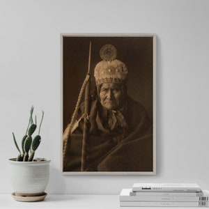 May include: A sepia-toned photograph of an Indigenous man wearing a feathered headdress and traditional clothing. He is looking directly at the camera with a serious expression.