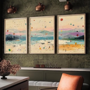 May include: Three framed abstract landscape paintings. Each artwork depicts a beach scene with colourful dots and brushstrokes. The paintings are framed in light wood and hang on a textured green wall. The overall theme is coastal.