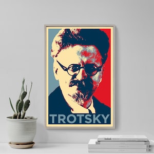 May include: A framed poster featuring a stylized portrait of Leon Trotsky. The image uses a red, blue, and beige color scheme, with the name "TROTSKY" in bold white letters at the bottom. The portrait shows a man with glasses and a mustache.
