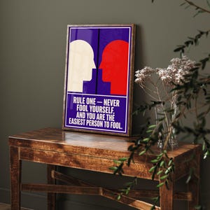Könnte beinhalten: Ein rechteckiges gerahmtes Wandbild mit tiefblauem Hintergrund und zwei einander zugewandten Profilsilhouetten in Weiß und Rot. Unter den Silhouetten steht in weißer Schrift: RULE ONE — NEVER FOOL YOURSELF, AND YOU ARE THE EASIEST PERSON TO FOOL.