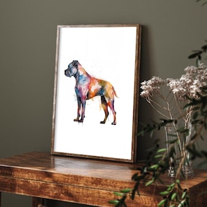 May include: A framed watercolor print of a Boxer dog. The dog is depicted in a side profile, with a vibrant mix of colors including blue, orange, yellow, and purple. The artwork is displayed on a wooden table.
