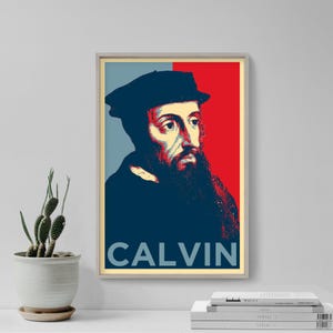 May include: A framed poster featuring a portrait of John Calvin with a beard and hat, set against a red and blue background. The word "CALVIN" is printed in white at the bottom of the image. The artwork is displayed on a white surface.