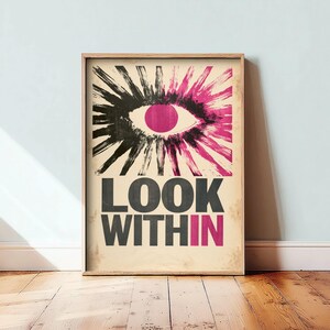 May include: A rectangular wall art print featuring a stylized eye with a pink pupil and radiating black and pink brushstroke lashes. Below the eye, the text reads LOOK WITH IN, with the letters IN highlighted in pink on a light beige background.
