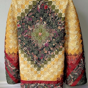 May include: A long-sleeved quilted jacket featuring a patchwork design with a central dark green floral pattern surrounded by yellow, red, and black geometric and paisley fabric blocks. The garment has a collar and a repeating stitched star pattern.