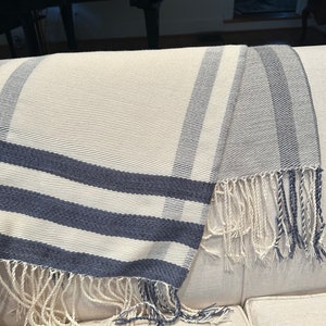 May include: A white and blue striped throw blanket with fringe. The blanket is folded and draped over a couch.