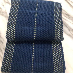 May include: A folded rectangular textile featuring a deep navy blue waffle weave texture. The fabric is accented with vertical stripes of a lighter, pale yellow-green color, creating a grid-like pattern across the surface of the material.