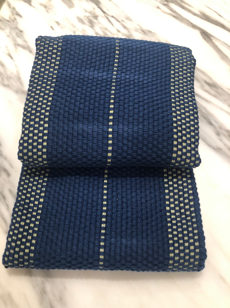May include: A folded rectangular textile featuring a deep navy blue waffle weave texture. The fabric is accented with vertical stripes of a lighter, pale yellow-green color, creating a grid-like pattern across the surface of the material.