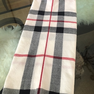May include: A white scarf with black and red plaid pattern. The scarf has a fringe on the bottom.
