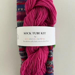May include: A sock tube kit with a vibrant pink yarn skein and a colorful sock tube. The sock tube features a striped pattern in shades of purple, blue, red, and green. The kit includes a label that reads "SOCK TUBE KIT by COLORFUL CROWNS".