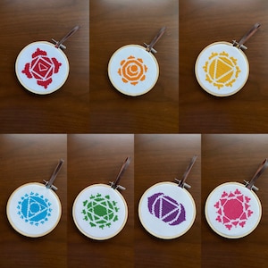 Puede incluir: Ocho aros bordados con símbolos de chakras de diferentes colores. Los símbolos son rojo, naranja, amarillo, verde, azul, índigo, violeta y rosa. Los aros son todos del mismo tamaño y están hechos de madera.
