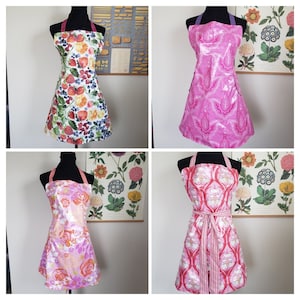 May include: Four different aprons with floral patterns. The aprons are pink, red, and white with floral designs. The aprons are on mannequins and are displayed against a white background.