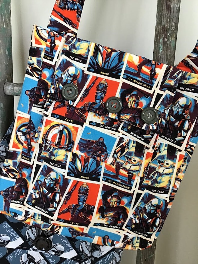 Puede incluir: Una bolsa de tela colorida con un patr&oacute;n repetido de personajes y texto de Star Wars. Los personajes incluyen The Mandalorian, The Child, IG-11 y The Armorer. El texto incluye "Mando", "The Mandalorian", "The Child", "IG-11", "The Armorer" y "Incinerator".