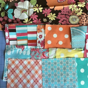 May include: A collection of fabric squares in various patterns and colors, including orange, blue, pink, and white. The fabrics are arranged in a grid pattern on a cutting mat.