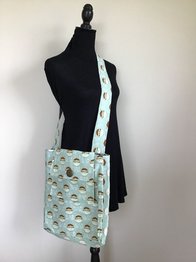 Puede incluir: Una bolsa de tela azul claro con un patr&oacute;n repetido de un personaje verde con el texto "He hablado" en ella. La bolsa tiene una correa marr&oacute;n con el mismo patr&oacute;n.