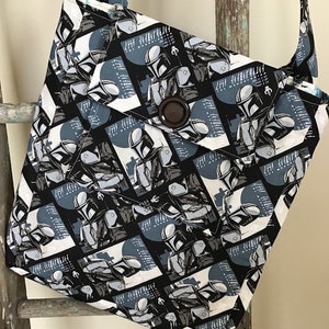 Puede incluir: Una bolsa de tela negra y blanca con un patr&oacute;n repetido de un personaje de la franquicia Star Wars. El personaje lleva un casco y una armadura. La bolsa tiene un cierre de bot&oacute;n &uacute;nico.