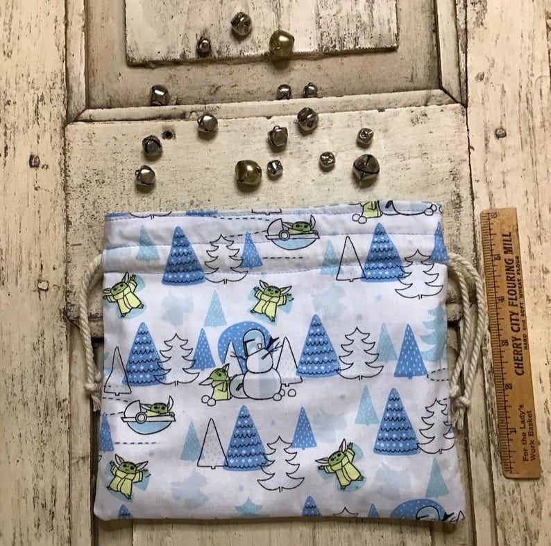 Op de afbeelding: Een witte trekkoordtas met een blauw en groen patroon van een populair fictief personage en kerstboom. De tas is gevuld met kleine zilveren belletjes.