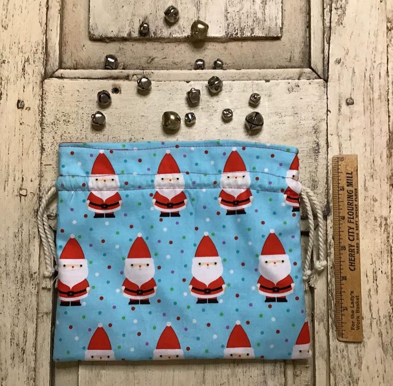 Op de afbeelding: Een blauwe trekkoordtas met een herhalend patroon van kerstmanfiguren en kleurrijke stippen. De tas is gemaakt van stof en heeft een wit trekkoord.