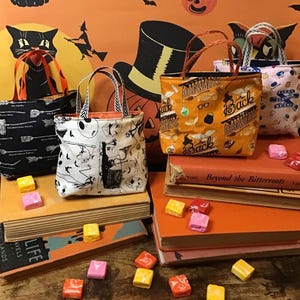 May include: Four Halloween-themed fabric trick-or-treat bags with different designs. The bags are arranged on a stack of books with sweets scattered around them. The bags feature designs of broomsticks, ghosts, and the words "Back to Hogwarts".