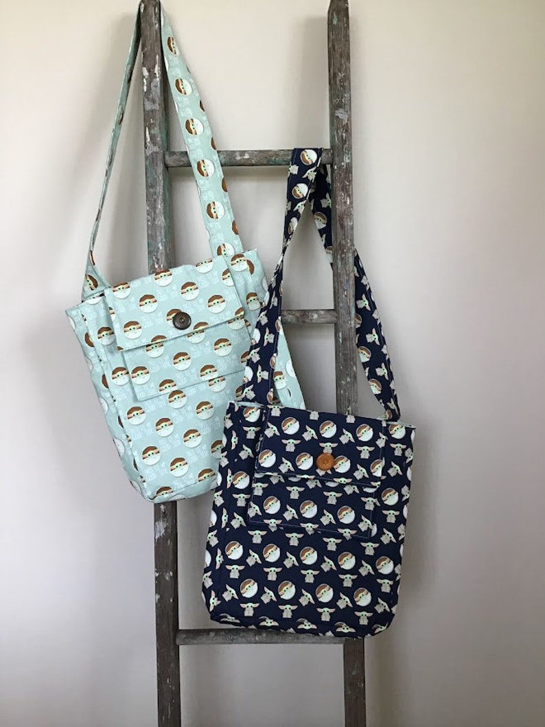 Puede incluir: Dos bolsas de tela con un patr&oacute;n de un personaje de dibujos animados. Una bolsa es azul claro con fondo blanco y la otra es azul oscuro con fondo blanco.