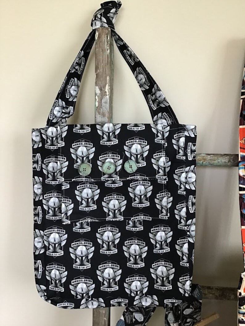 Puede incluir: Bolsa de tela negra con un patr&oacute;n repetido del casco de Mandalorian y el texto "The Mandalorian This is the Way".